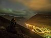 The lights from the town of Seyðisfjörður, which nestles amidst glorious mountains and ocean, and the glow of the Aurora Borealis in the clouds above.